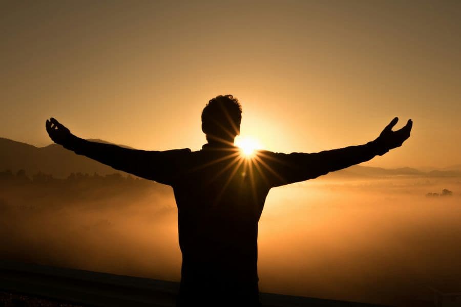 Mensch mit ausgebreiteten Armen im Sonnenaufgang
